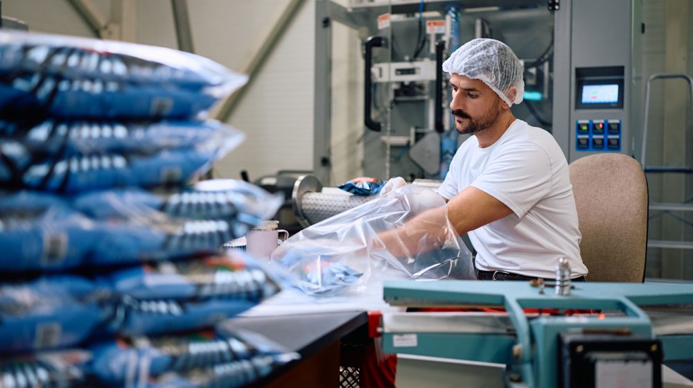 Factory employee packing processed food while working in production facility. Factory employee packing processed food while working in production facility.